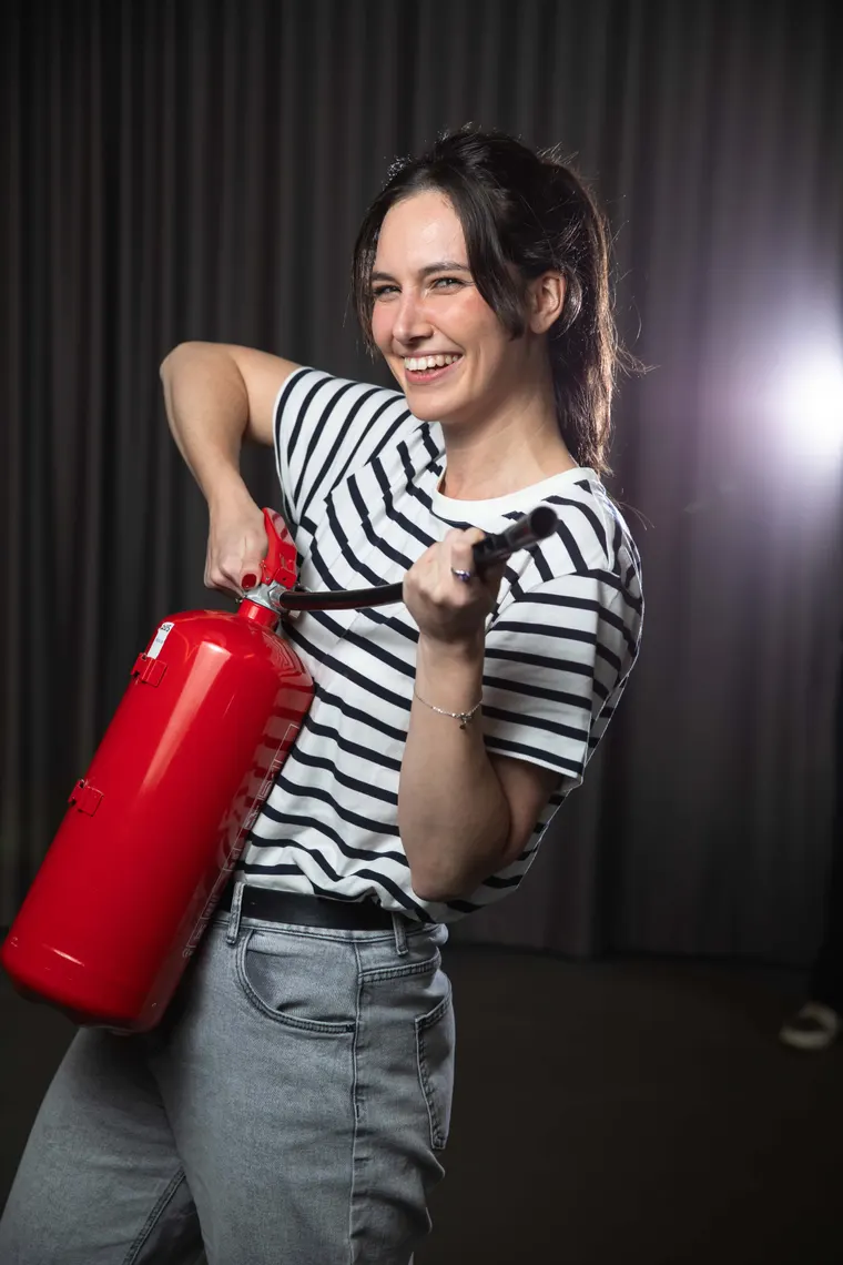 Tess holding a red fire extinguisher, ready to put out your French panic
